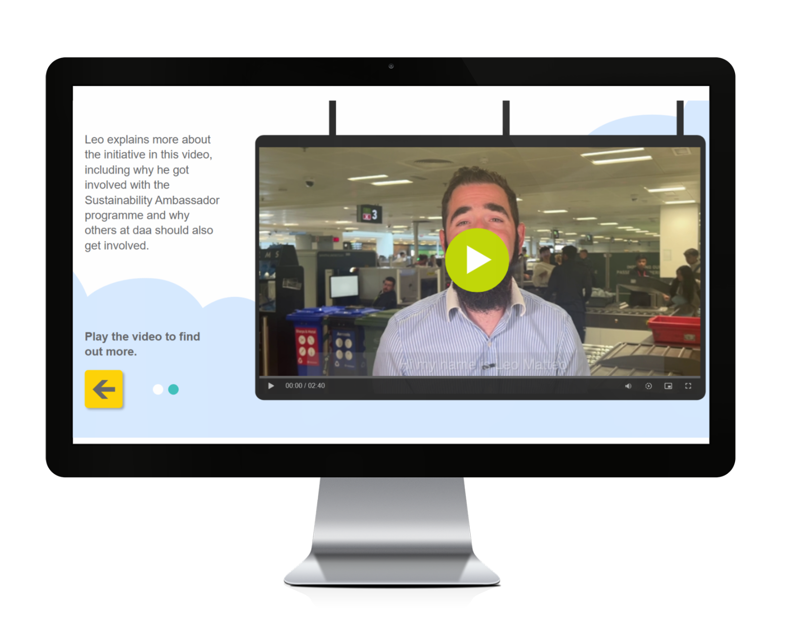 A desktop computer monitor displaying an eLearning video module featuring Leo, a Sustainability Ambassador at daa. The screen shows a video player with a man in a striped shirt speaking directly to the camera from what appears to be an airport office environment, with workstations and colleagues visible in the background. The video has a prominent green play button overlay and shows a duration of 02:40.
On the left side of the screen, there is explanatory text that reads "Leo explains more about the initiative in this video, including why he got involved with the Sustainability Ambassador programme and why others at daa should also get involved." Below this text is a call-to-action stating "Play the video to find out more."
The interface includes navigation elements with a yellow back arrow button and a teal progress indicator dot. The overall design uses a clean, modern layout with light blue accent elements and maintains the professional aesthetic consistent with corporate training materials. The video appears to be part of a larger sustainability training programme designed to engage airport employees in environmental initiatives.