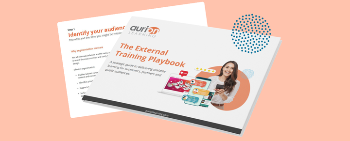 A graphic mockup of a printed booklet titled "The External Training Playbook" by Aurion Learning, set at an angle against a light peach background. The front cover displays the title alongside a graphic of a smiling woman holding a smartphone and UI elements. Peeking out behind the booklet is an open interior page showing a section titled "Step 1: Identify your audience," with text discussing audience segmentation.